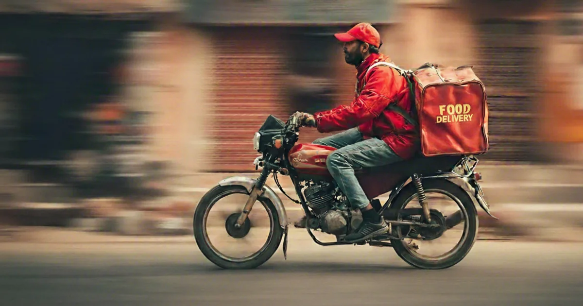 Food delivery courier on bicycle with insulated delivery bag riding through city street